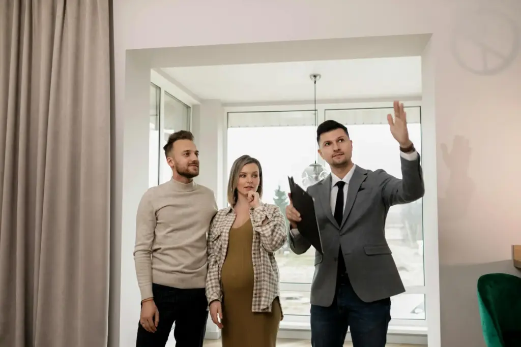 Mit einer Suchanzeige zum Erfolg bei der Wohnungssuche? Das Bild zeigt einen Makler, der einem Paar eine Wohnung zeigt nachdem sie eine Suchanzeige geschaltet haben